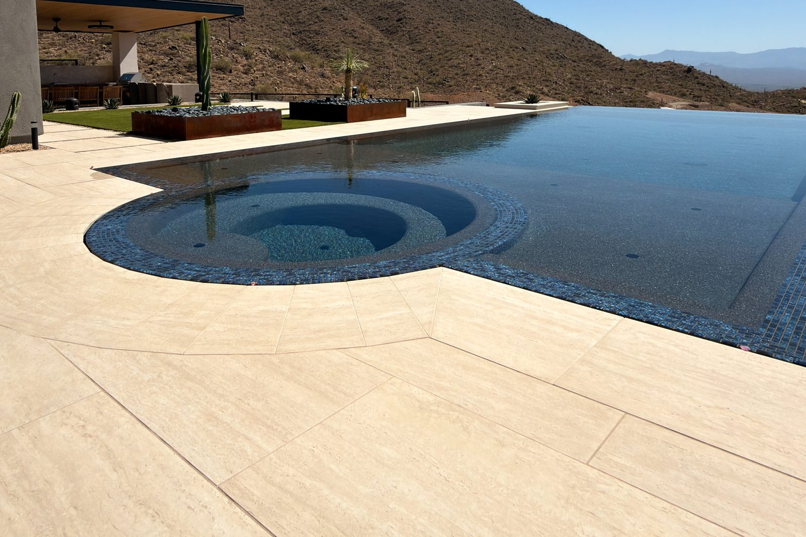 Large-format porcelain pavers in a travertine finish surrounding a spa and negative-edge pool