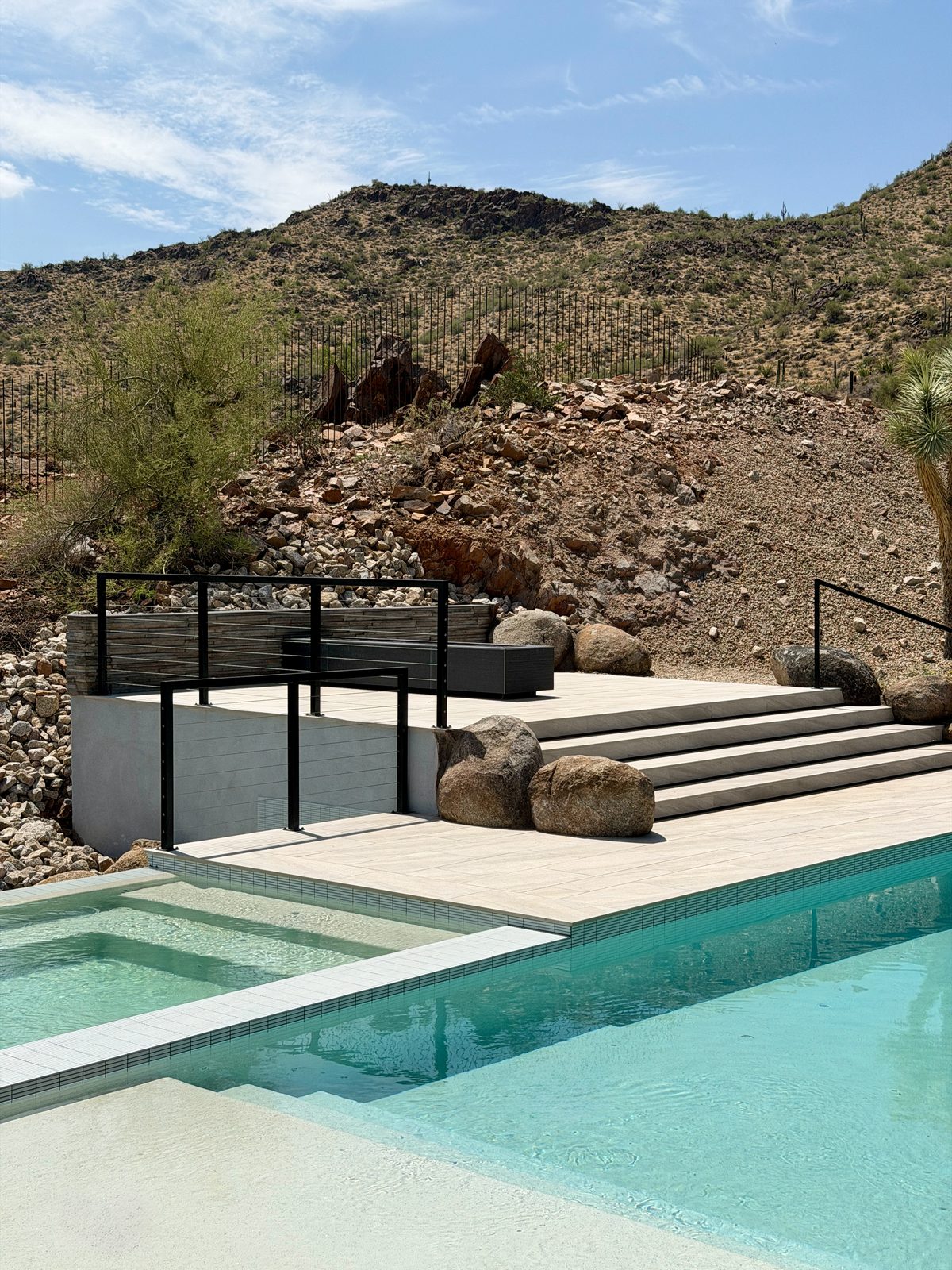 Pool and raised spa with stone steps against a desert hillside