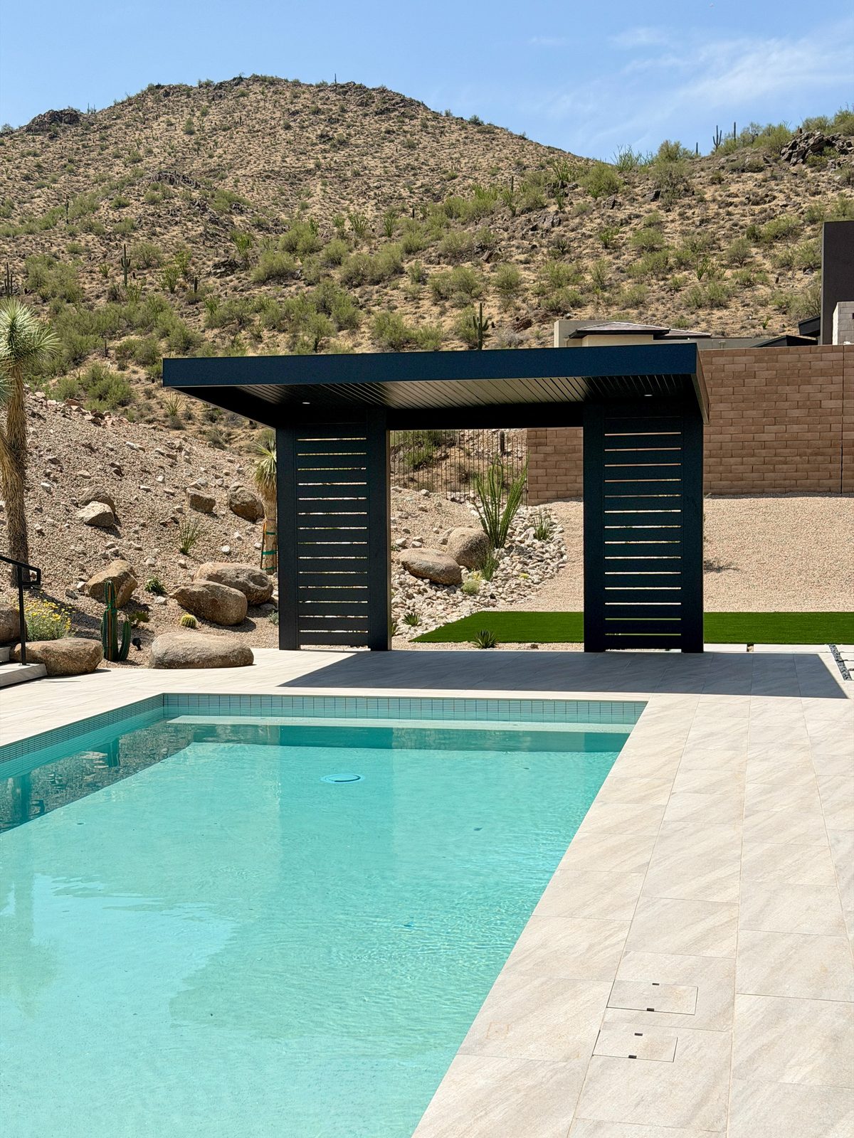 Pool with black louvered shade structure and turf beyond